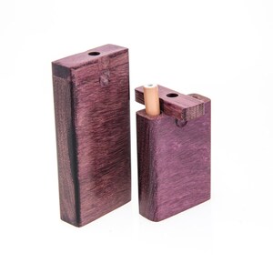 May include: Two wooden boxes with lids, one slightly larger than the other. Both boxes are a deep purple color with a wood grain pattern. The smaller box has a small wooden dowel sticking out of the top.