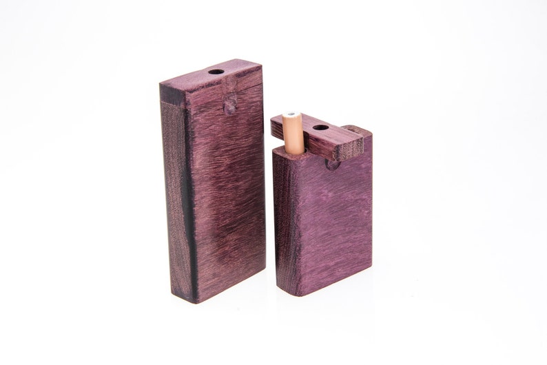 May include: Two wooden boxes with lids, one slightly larger than the other. Both boxes are a deep purple color with a wood grain pattern. The smaller box has a small wooden dowel sticking out of the top.