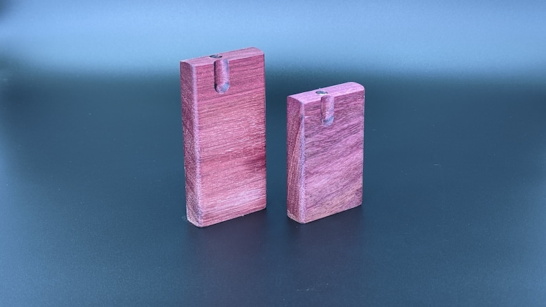 May include: Two wooden smoking pipes, one larger than the other, are made of a dark reddish-purple wood. The pipes are both rectangular in shape and have a small hole at the top.