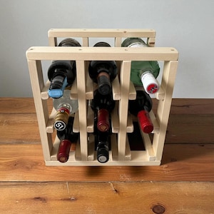 May include: A natural wood wine rack holding several wine bottles. The rack is constructed with a grid-like design, allowing for the storage of multiple bottles. The bottles are of various colors, with visible labels. The rack sits on a wooden surface.
