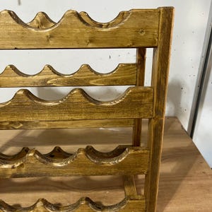 May include: A wooden wine rack with a warm, golden-brown finish. The rack has multiple curved shelves designed to hold wine bottles. The construction appears sturdy, with vertical supports and a classic design. The rack is suitable for home storage.