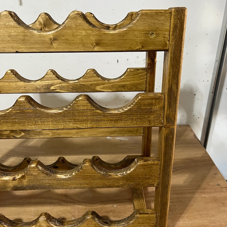 May include: A wooden wine rack with a warm, golden-brown finish. The rack has multiple curved shelves designed to hold wine bottles. The construction appears sturdy, with vertical supports and a classic design. The rack is suitable for home storage.