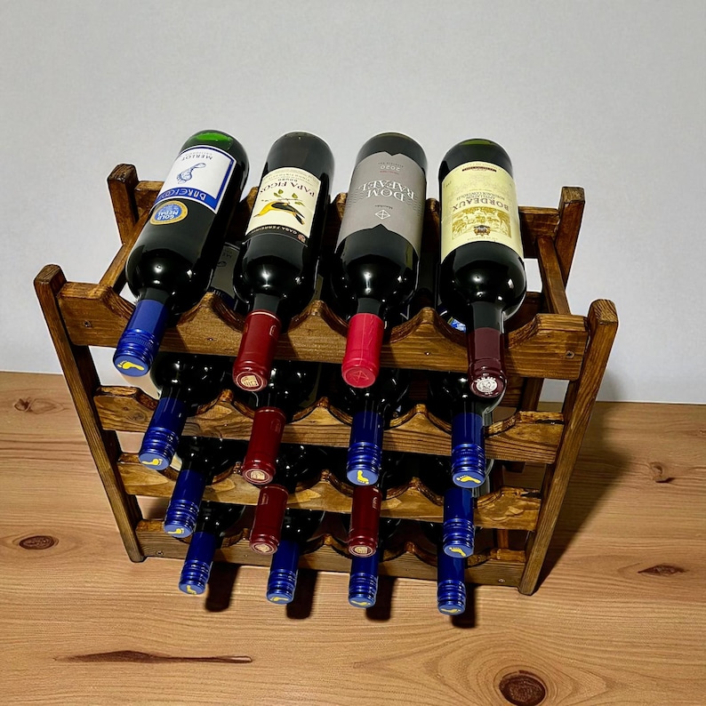 May include: A wooden wine rack holding twelve bottles of wine. The rack is stained a medium brown and has a tiered design. The wine bottles are various colors, with red and blue bottle caps.