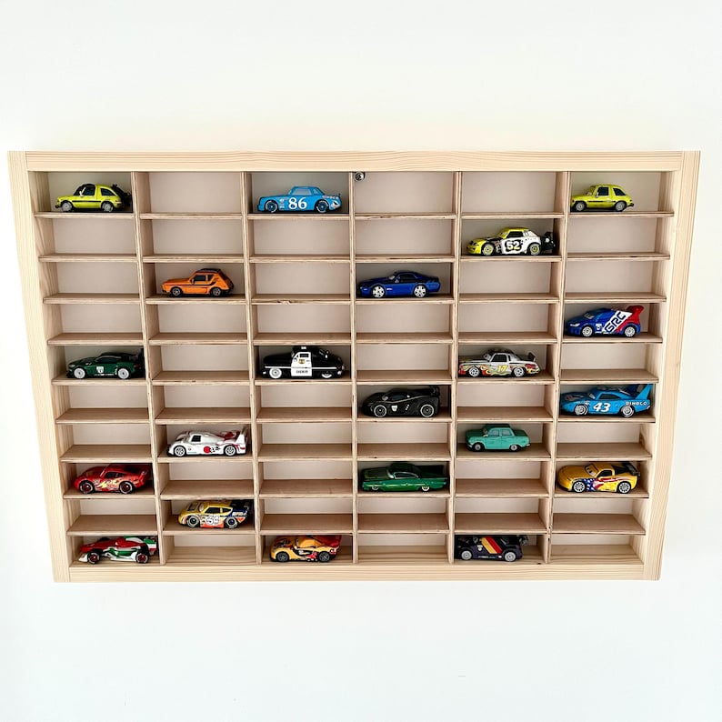 May include: A wooden display case with multiple compartments, filled with a collection of colorful toy cars. The cars are various models and colors, including blue, yellow, red, and green. The case is made of light-colored wood.