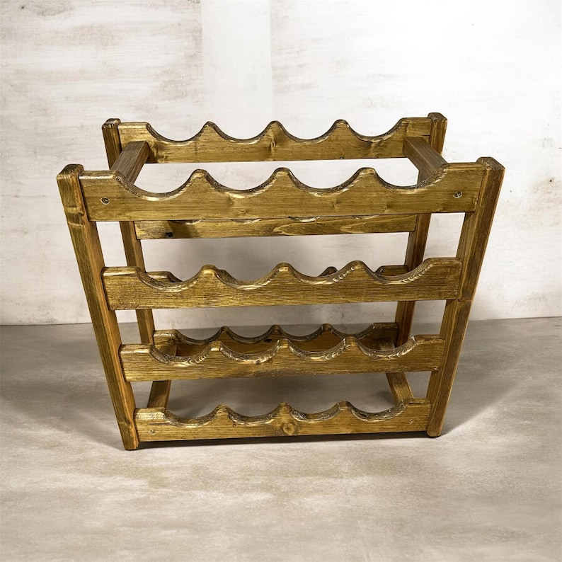 May include: A wooden wine rack with a golden finish. The rack is designed to hold multiple bottles, with scalloped edges on each shelf. The structure is angled for stability and has a rustic aesthetic.