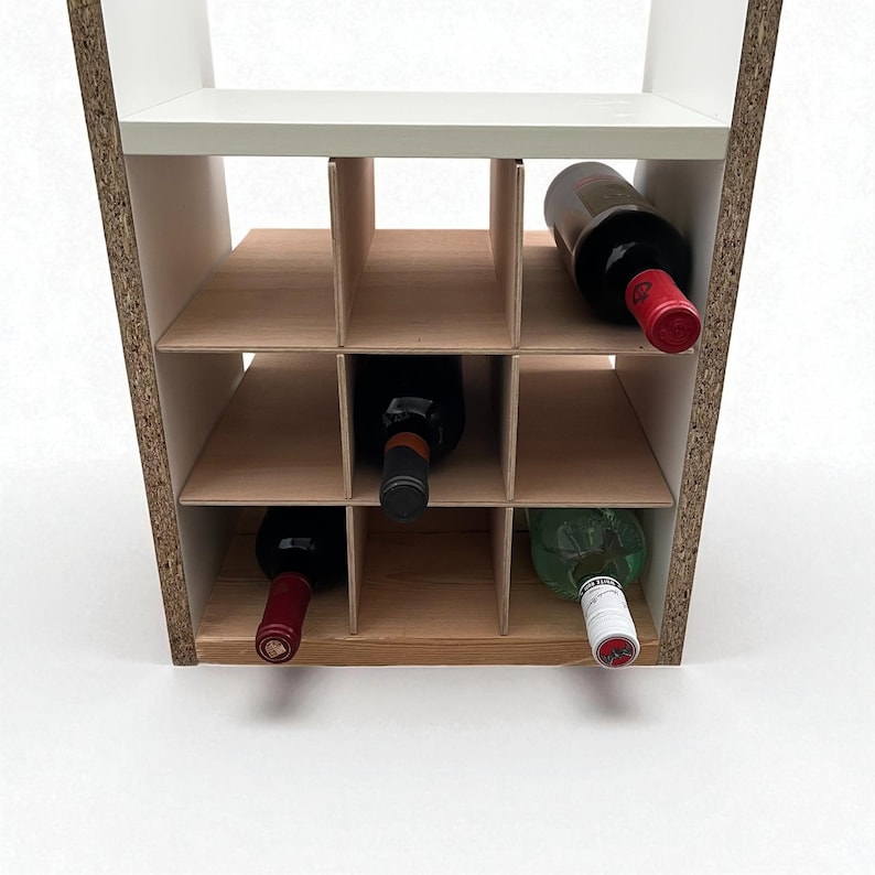 May include: A wooden wine rack with a white top shelf and nine compartments. Several wine bottles are stored in the rack, with red and green bottles visible. The rack is made of light brown wood and has a modern design.