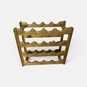 May include: A wooden wine rack with a golden finish. The rack is designed to hold multiple bottles, with curved slots to cradle each bottle. The rack has a rectangular shape and is made of wood.