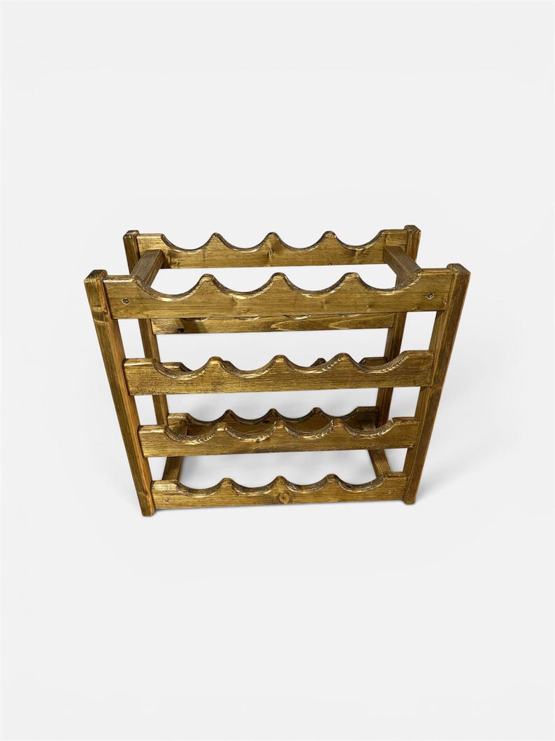 May include: A wooden wine rack with a golden finish. The rack is designed to hold multiple bottles, with curved slots to cradle each bottle. The rack has a rectangular shape and is made of wood.