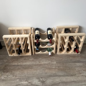 May include: Multiple wooden wine racks, each holding several bottles of wine. The racks are made of light-colored wood and have a geometric design. Some bottles are visible, with red and white labels.