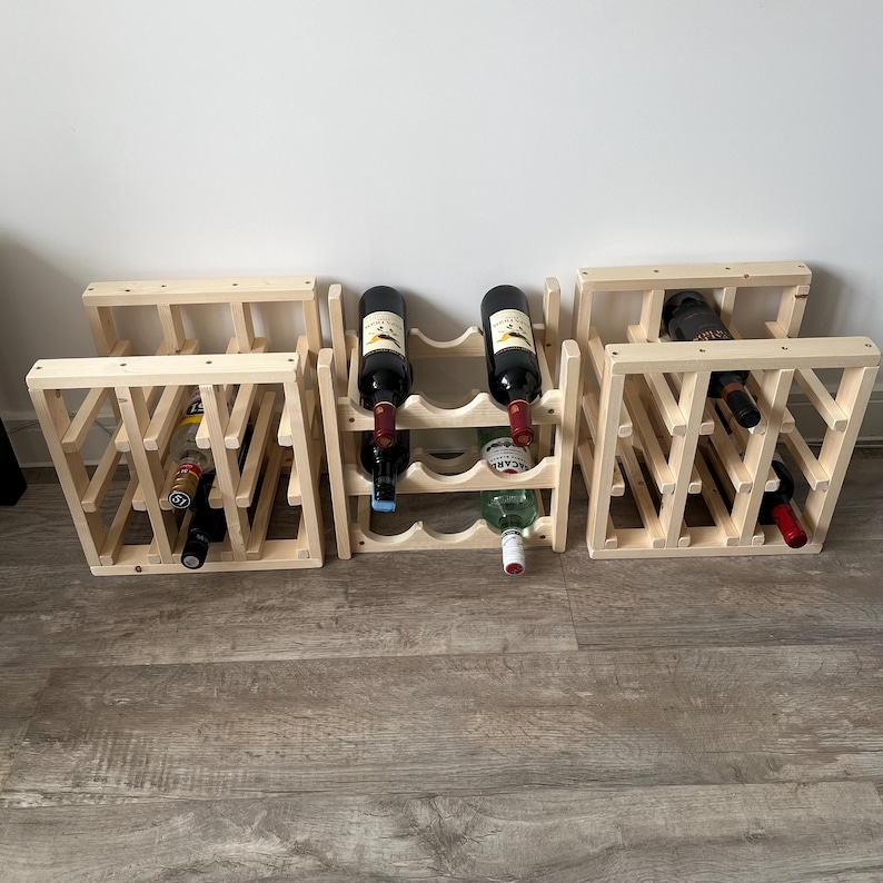 May include: Multiple wooden wine racks, each holding several bottles of wine. The racks are made of light-colored wood and have a geometric design. Some bottles are visible, with red and white labels.