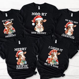 May include: Black t-shirts with Christmas cow graphics. Each shirt features a cow wearing a Santa hat and holding presents, with phrases like "Give me an udder present" and "Moo-ry and bright."