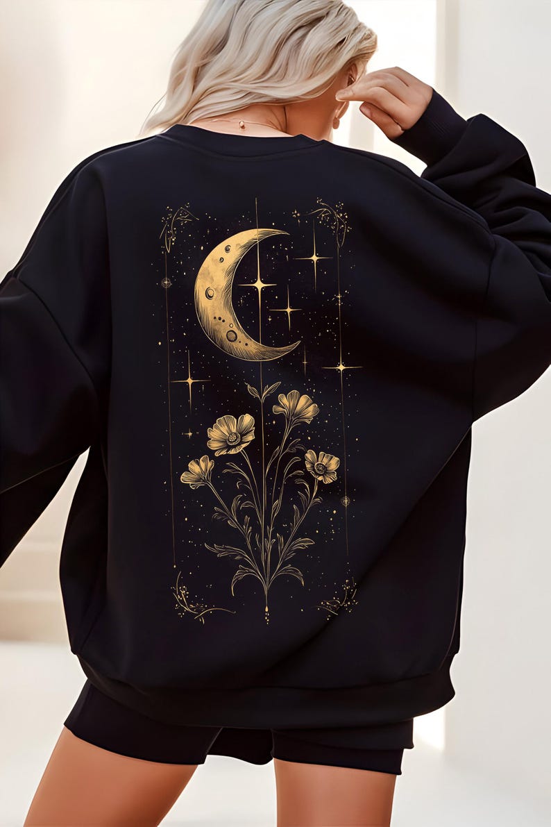 May include: Black sweatshirt featuring a celestial design. The back of the sweatshirt displays a gold crescent moon, stars, and floral elements. The design is detailed with gold accents, creating a striking contrast against the black fabric.