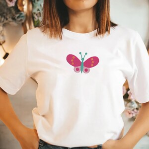 May include: White t-shirt with a pink butterfly embroidered on the front. The butterfly has orange and green accents.