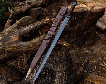 May include: A medieval-style sword with a brown leather-wrapped handle and a silver blade, resting on a wooden surface. The sword is accompanied by a brown leather sheath. The image has the text "ABBUTTCRAFT".