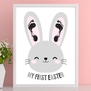 May include: A white frame with a gray bunny rabbit with pink ears and black footprints. The bunny has a happy face and the text "My First Easter" is below the bunny.