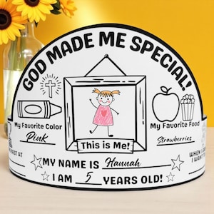 以下が含まれることがあります： 「GOD MADE ME SPECIAL!」と「MY NAME IS Hannah」の文字が入った白い紙の王冠。王冠には女の子の絵、クレヨン、リンゴ、ポップコーンが描かれています。「I AM 5 YEARS OLD!」とも書かれています。