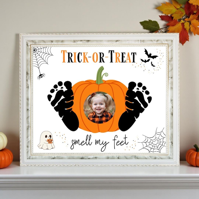 May include: A framed Halloween-themed print with a white border. The print features a pumpkin with a child's photo in the center, black footprints, spiderwebs, bats, and the text "TRICK-OR-TREAT" and "smell my feet".