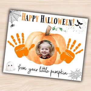 Può includere: Un biglietto a tema Halloween con un design a zucca. Il biglietto presenta il testo "HAPPY HALLOWEEN!" in arancione e nero, con la foto di un bambino al centro. Impronte di mani arancioni incorniciano la zucca e il testo "from your little pumpkin" è scritto sotto.