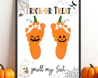 May include: A framed Halloween-themed print featuring orange footprint pumpkins with jack-o'-lantern faces. The words "TRICK-OR-TREAT" and "smell my feet" are written on the white background. Includes a ghost holding a pumpkin, bats, and spiderwebs.
