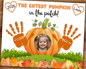 May include: A rectangular sign featuring the text THE CUTEST PUMPKIN in the patch! with a central orange pumpkin illustration containing a circular photo of a child. Two orange handprints flank the pumpkin, with hearts labeled 2026 and Layla.