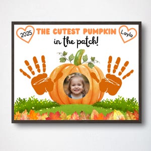 May include: A framed print featuring a pumpkin design with a child's photo in the center. The text reads "THE CUTEST PUMPKIN in the patch!" with the name "Layla" and the year "2025" in heart-shaped accents. Orange handprints and autumn leaves complete the design.