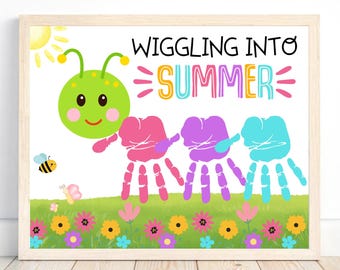 May include: A framed print with a whimsical summer theme. It features a green caterpillar with handprint feet, the words "Wiggling Into Summer," and a colorful garden scene with a sun, bee, and flowers. The artwork is set against a white background.