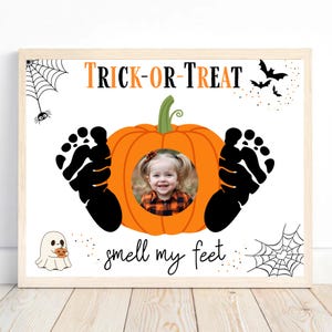 May include: Halloween-themed framed print with the words "Trick-or-Treat" in orange and black. A smiling child's photo is centered in an orange pumpkin, flanked by black footprints. Additional graphics include bats, spiders, and the phrase "smell my feet."