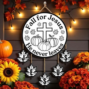 May include: A round wooden sign with the text "Fall for Jesus He never leaves" in black and white. The sign features a cross, pumpkins, and leaf accents. Decorative leaves spell out "JESUS" below. The sign is hanging on a wooden wall with fall foliage.