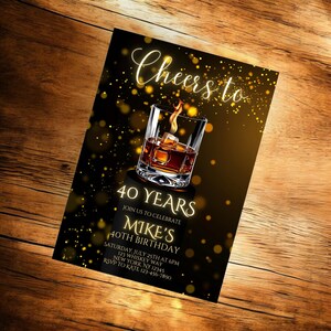 Pode incluir: Um convite de anivers&aacute;rio preto e dourado com um copo de u&iacute;sque e gelo. O texto diz "Cheers to 40 Years. Join us to celebrate Mike's 40th Birthday. Saturday, July 25th at 6pm. 123 Whiskey Way, New York, NY 12345. RSVP to Kate 123-456-7890."