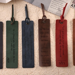 Könnte beinhalten: Eine Sammlung von sechs Leder-Lesezeichen in verschiedenen Farben, jeweils mit einer Lederschlaufe und geprägtem Text. Die Farben umfassen Dunkelgrau, Grün, Blau, Braun, Rot und Hellbraun. Die Lesezeichen enthalten inspirierende Zitate und personalisierte Namen.