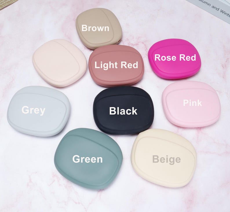 Op de afbeelding: Een verzameling van negen beschermhoezen voor oordopjes in verschillende kleuren, waaronder bruin, lichtrood, rozerood, grijs, zwart, roze, groen en beige. Elke hoes heeft een afgeronde vorm met de kleurnaam erop.