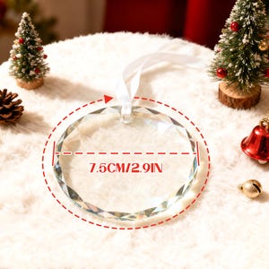 May include: A clear, circular, faceted glass ornament with a white ribbon loop for hanging. The ornament features a printed measurement graphic indicating a diameter of 7.5 cm or 2.9 inches, centered on the glass surface.