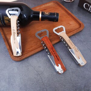 May include: Three personalized wine bottle openers with wooden handles and stainless steel accents. One opener rests on a wooden tray with a wine bottle. Each opener has custom text, including names and dates.