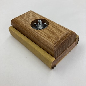 May include: A wooden sanding block with a metal screw and a piece of sandpaper attached to the bottom.