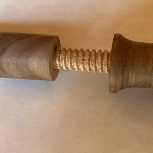 May include: A wooden pepper grinder with a cylindrical body and a screw mechanism. The grinder is made of a light brown wood with visible grain, and the screw is a lighter color. The handle is a rounded shape.