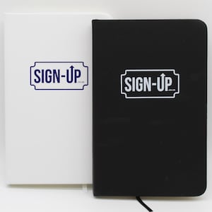 Könnte beinhalten: Zwei Notizbücher, eines weiß und eines schwarz, stehen nebeneinander vor einem weißen Hintergrund. Jedes Notizbuch trägt den Text "SIGN-UP" in einem blau-weißen Design. Das schwarze Notizbuch hat ein schwarzes Leseband.