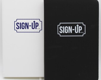 May include: Two notebooks, one white and one black, stand side-by-side against a white background. Each notebook features the text "SIGN-UP" in a blue and white design. The black notebook has a black ribbon bookmark.