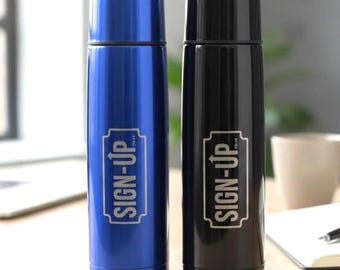 May include: Two insulated stainless steel water bottles, one blue and one black, with the text "SIGN-UP" in a rectangular frame. The bottles are cylindrical with a rounded top and are on a wooden desk.