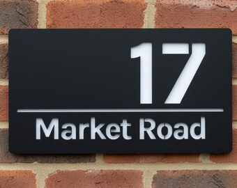 May include: A black rectangular address sign with the number "17" in white, and the words "Market Road" below. The sign is mounted on a red brick wall.