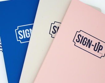 May include: A collection of notebooks in white, blue, beige, and pink. Each notebook has the words "SIGN-UP" printed in a dark blue, retro-style design. The notebooks are arranged in a fan shape, with the covers visible.