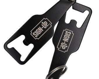May include: Two black bottle openers with key rings. Each opener has a bottle cap remover and the text "SIGN-UP" in a white rectangular box. The openers are made of metal and are on a white background.