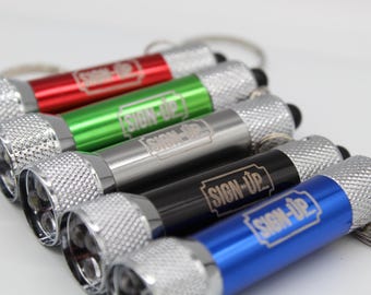 May include: A collection of small flashlights in red, green, silver, black, and blue. Each flashlight has a silver textured head and the text "SIGN-UP" printed on the body. The flashlights are attached to keychains.