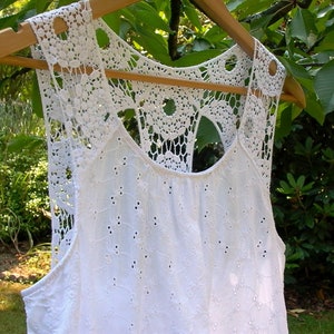 May include: White crochet top with a delicate lace design. The top has a scoop neck and a sleeveless design.