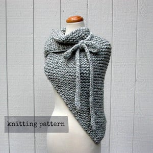 Puede incluir: Un chal gris tejido con forma triangular y un nudo en el cuello. El chal se muestra en un maniquí blanco. El texto "knitting pattern" es visible en la parte inferior de la imagen.