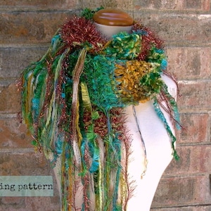 May include: A colorful scarf with a mix of green, brown, gold, and red yarn. The scarf is made with a chunky yarn and has a fringe on the ends. The scarf is displayed on a white mannequin.