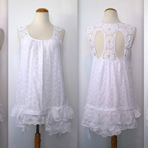 May include: White sleeveless dress with a lace overlay and a scalloped hem. The dress has a round neckline and a gathered bodice. The back of the dress features a cutout design.