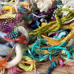 May include: A collection of assorted textile fibers, including various ribbons, yarns, and fabric strips in a vibrant mix of colors such as lime green, turquoise, gold, purple, and white, featuring diverse textures like metallic, fuzzy, and woven.