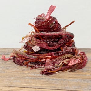 May include: A pile of decorative ribbon in shades of red, pink, and gold. The ribbon is layered and textured, with some sections featuring glitter and metallic threads. The arrangement is on a wooden surface.