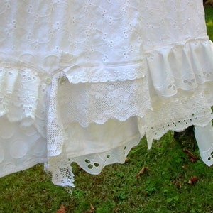 May include: White cotton fabric with multiple layers of lace trim. The fabric has a delicate eyelet pattern and is hanging on a clothesline.