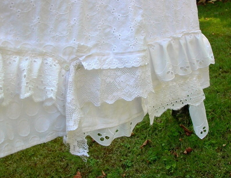 May include: White cotton fabric with multiple layers of lace trim. The fabric has a delicate eyelet pattern and is hanging on a clothesline.